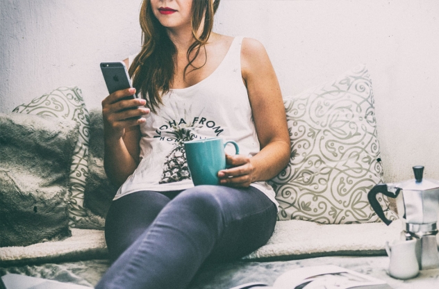 Frau schaut auf ihr Smartphone und trinkt Kaffe