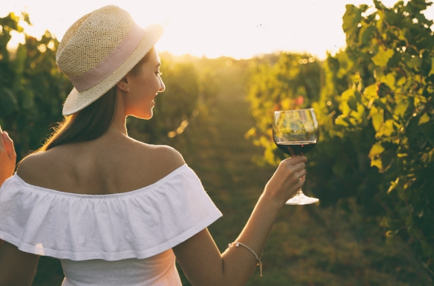 Frau hält Rotwein zwischen Weinreben