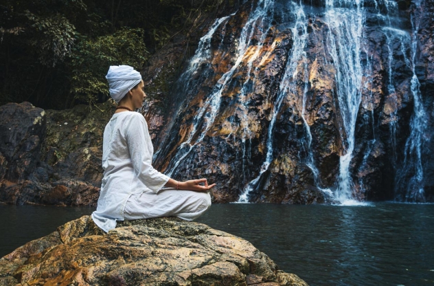 Frau meditiert auf einem Stein am Wasserfall