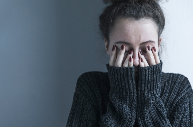 Frau versteckt ihr Gesicht hinter ihren Händen mit Generalisierte Angststörung