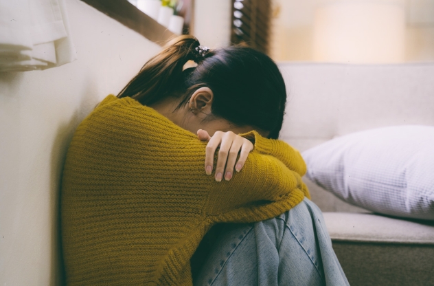 Mental Load Frau sitzt mit dem Kopf in den Schoß gelegt auf dem Boden