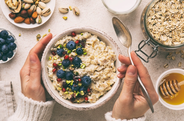 Blick von oben auf eine Schale mit Müsli und Beeren. Weitere Zutaten liegen verstreut im Bild. 