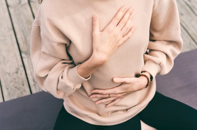 Yoga bei Depressionen Frau sitzt auf Yogamatte mit Händen auf Brust und Bauch