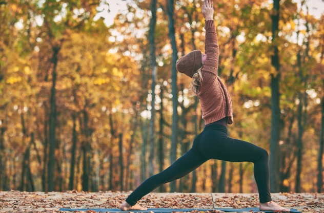 Frau macht in Herbstlandschaft Krieger 1 Yoga-Übung gegen Bluthochdruck