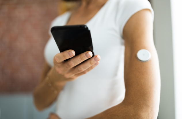 Eine Frau misst mit ihrem Handy und einem Sensor am Arm ihren Blutzucker