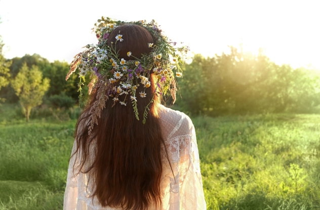 Frau von hinten mit Blumenkranz in den Haaren steht auf einer Wiese
