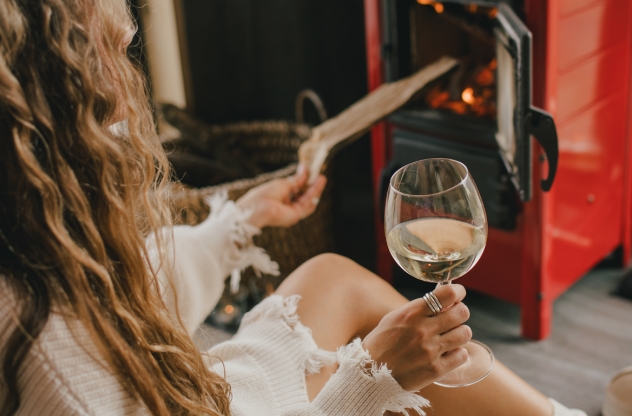 Eine Frau sitzt vor dem Kamin und hält ein Weinglas in der Hand | Leben ohne Alkohol