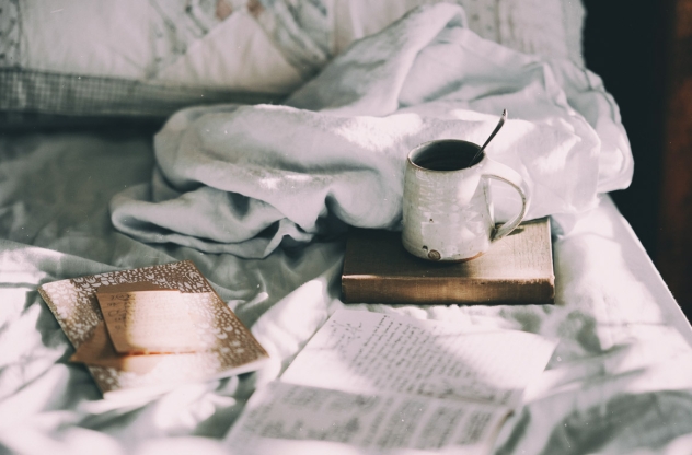 Morgenroutine: Tasse Kaffee steht auf einem Journal im Bett
