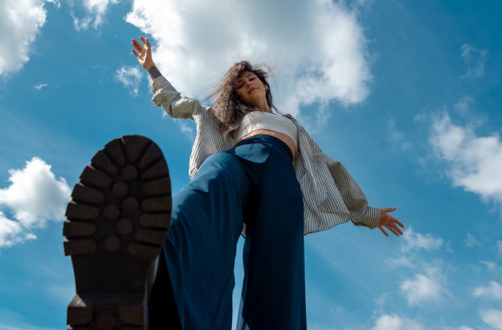 Quarterlife Crisis: Eine Frau, von unten vor blauem Himmel fotografiert, streckt Fuß nach vorne, die Arme ausgebreitet.
