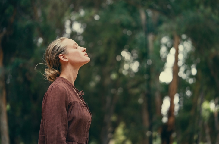 Frau mit geneigtem Kopf und geschlossenen Augen vor Waldhintergrund