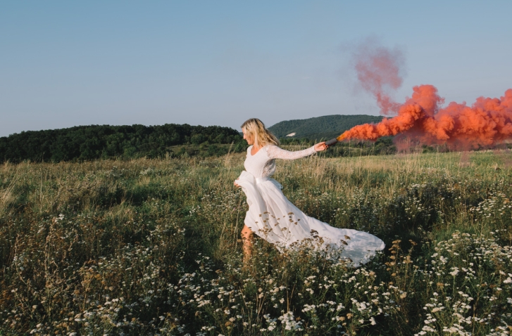 Frau in weißem Kleid rennt mit Kreidepulver in der Hand über eine Wiese