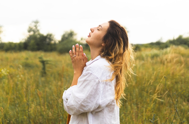Frau mit gefalteten Händen und geschlossenen Augen auf einer Wiese