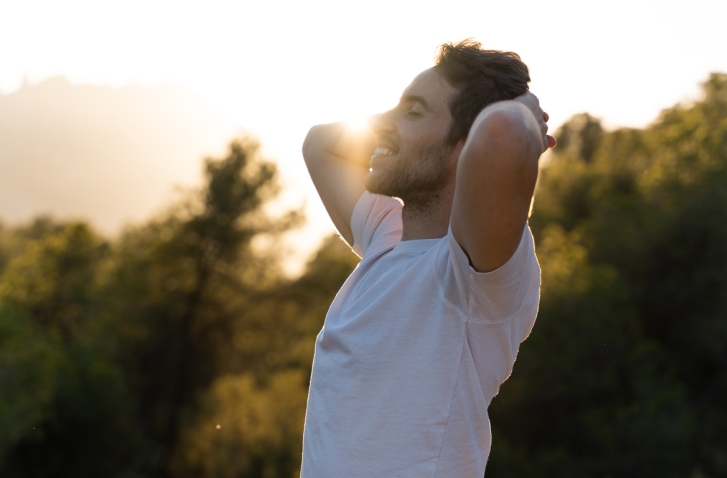Man mit verstränkten Armen hinter dem Kopf vor Waldhintergrund