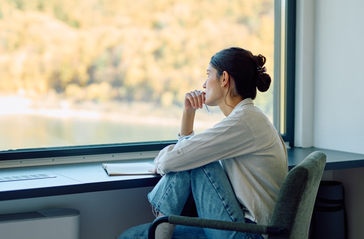 Frau mit angezogenen Beinen vor einem Fenster
