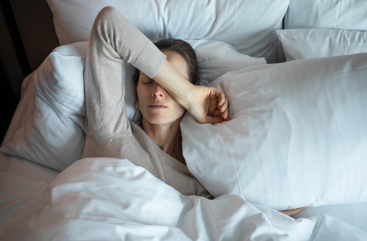 Frau liegt im Bett mit Arm über dem Gesicht