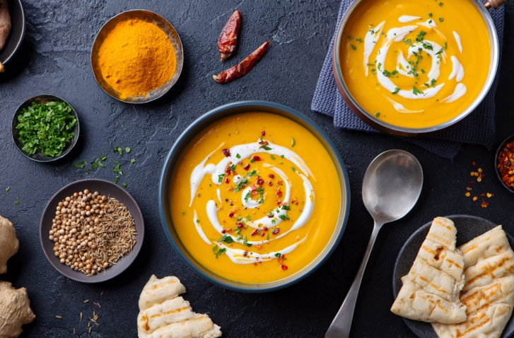 Schwarze Platte mit orangener Crèmesuppe und Gewürzschalen