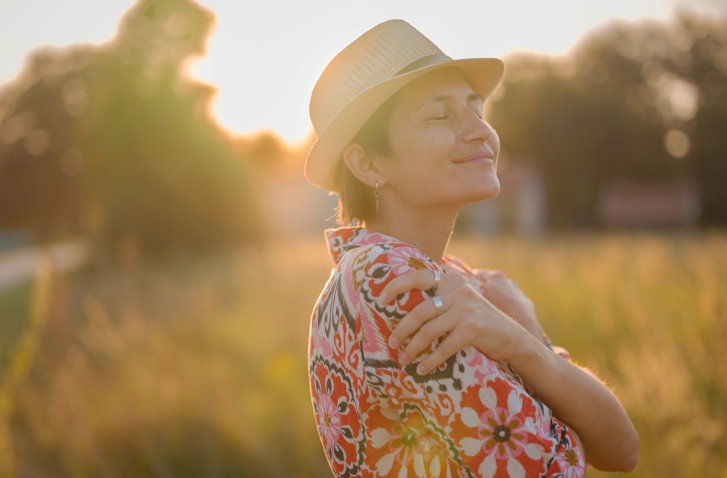 Frau die sich selbst umarmt vor Wiesenhintergrund