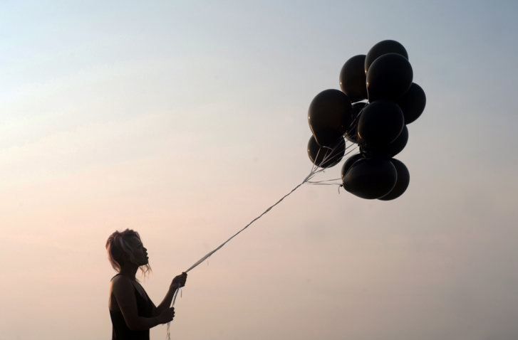 Seitenprofil einer Frau mit Luftballons in der Hand vor rosafarbenem Himmel