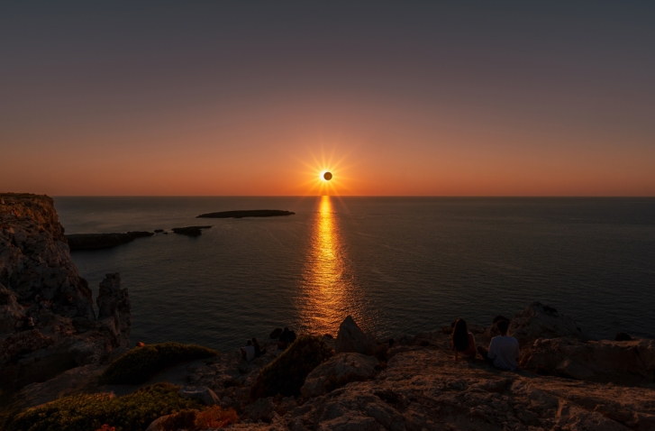 Sonnenuntergang im Zentrum des Horizontes mit schwarzem Kreis vor der Sonne vor einer Wasseroberfläche