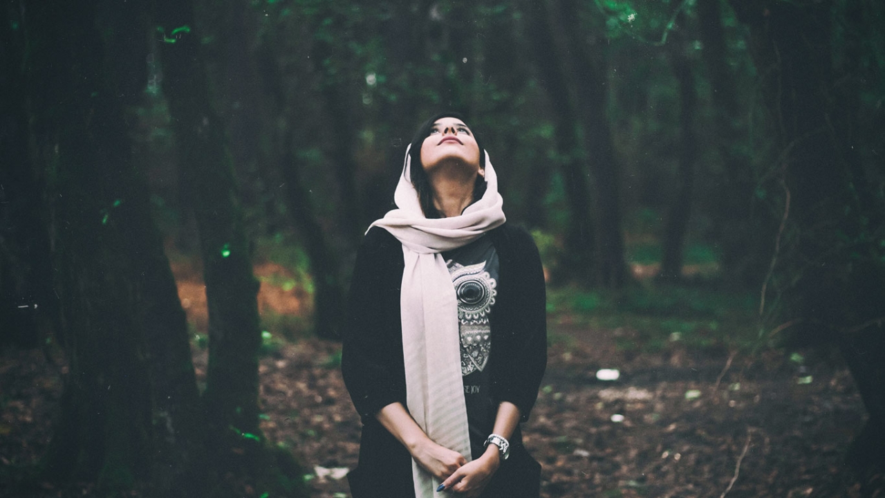 Entspannt leben: Eine Frau steht im Wald und blickt mit geschlossenen Augen nach oben.