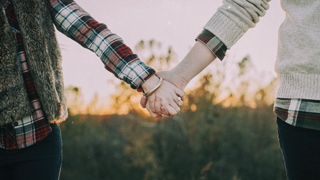 Selbstwertschätzung: Zwei Menschen halten sich an den Händen vor einem Sonnenuntergang.