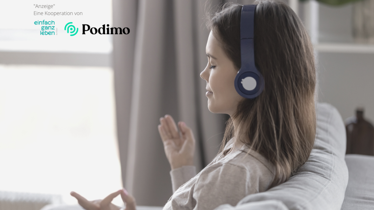 Eine Frau mit Kopfhörern meditiert auf dem Sofa