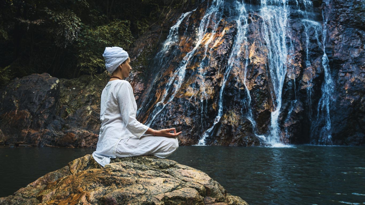 Frau meditiert am Wasserfall Frau meditiert auf einem Stein am Wasserfall