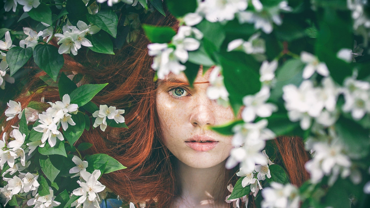 Frau schaut ängstlich hinter einem Busch hervor