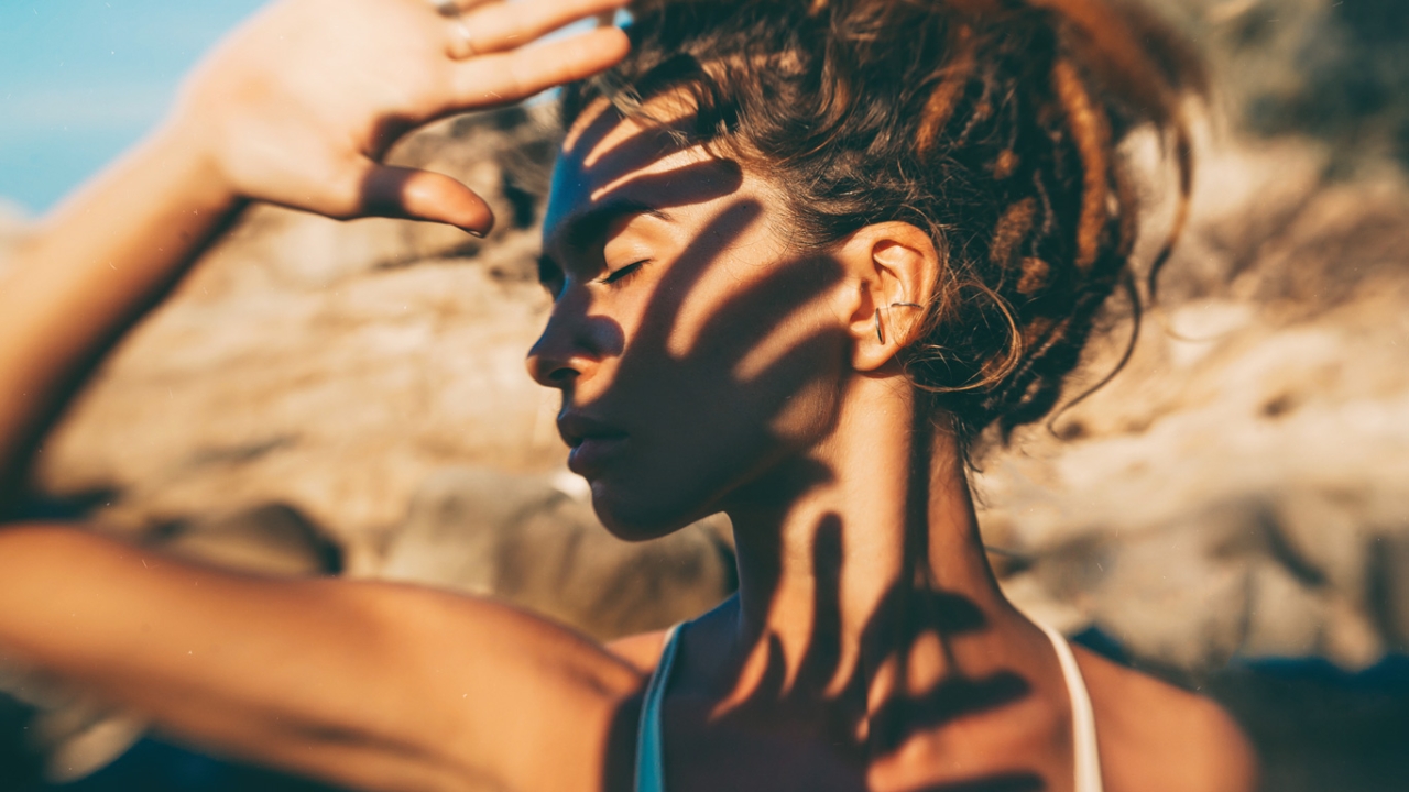 Frau hält sich Hand vors Gesicht, Schatten zeichnen sich auf ihrer Haut ab