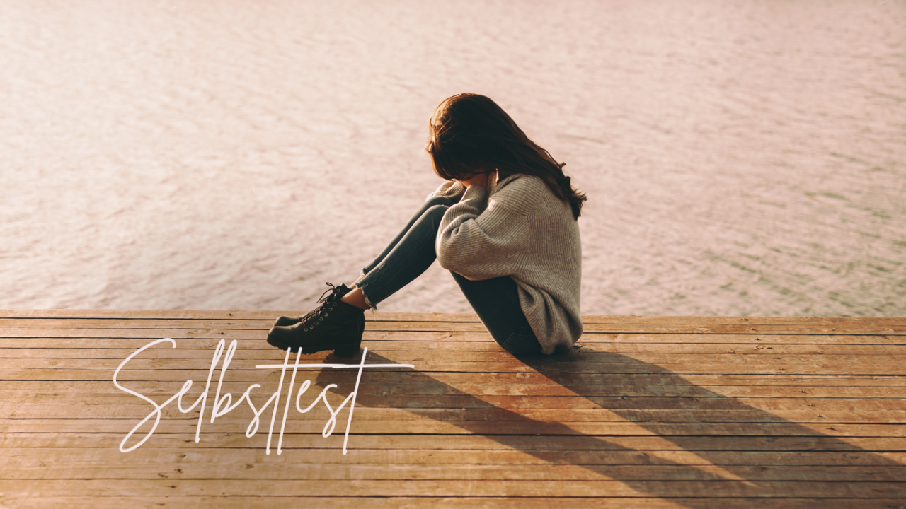 Zwangsstörung-Test: Frau sitzt am Seeufer auf Steg mit dem Gesicht in den Händen