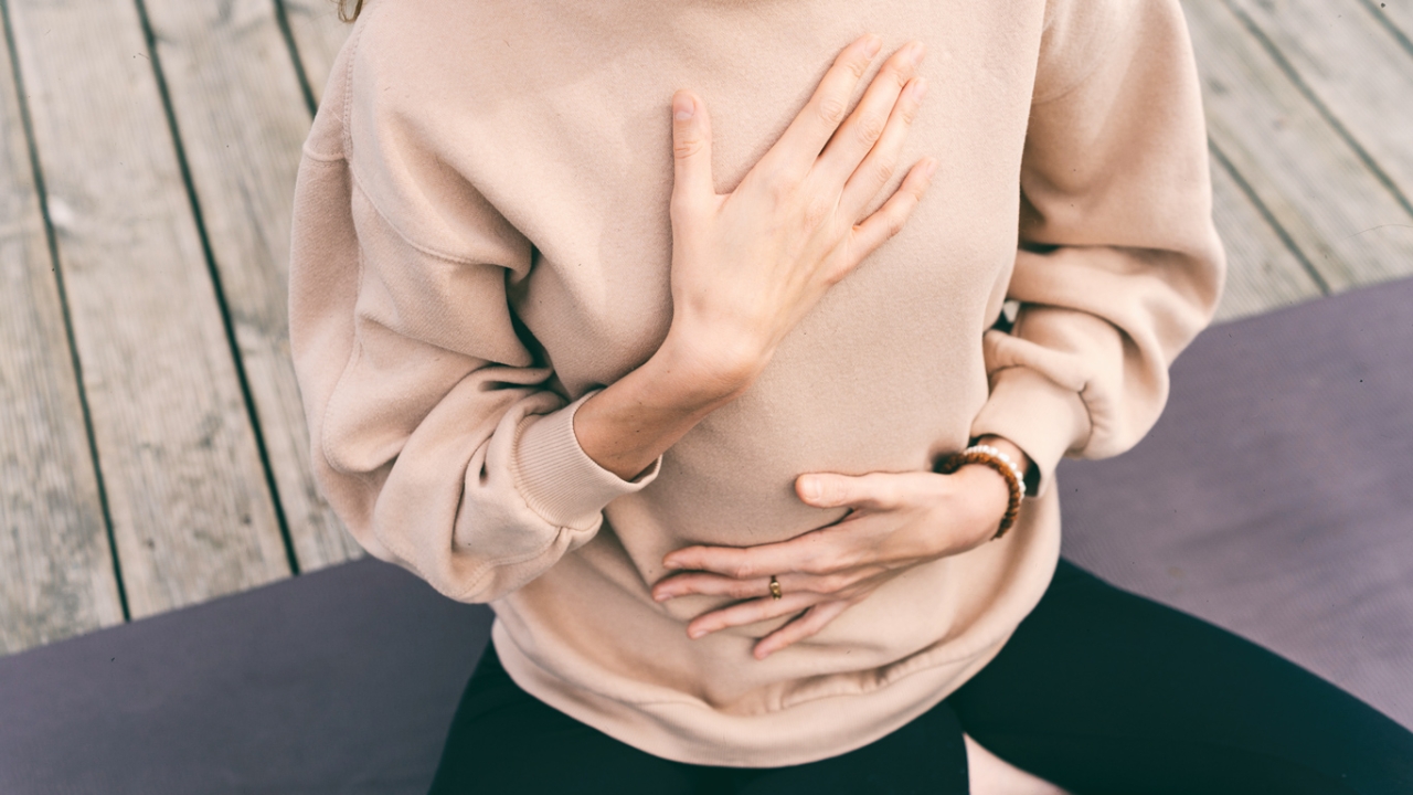 Yoga bei Depressionen Frau sitzt auf Yogamatte mit Händen auf Brust und Bauch Yoga bei Depressionen Frau sitzt auf Yogamatte mit Händen auf Brust und Bauch