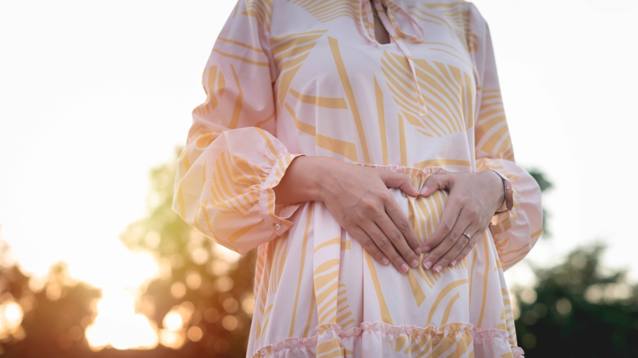 Frau umarmt ihren Bauch unerfüllter Kinderwunsch Frau in luftigem Sommerkleid umarmt ihren Bauch und formt ein Herz und hat einen unerfüllten Kinderwunsch