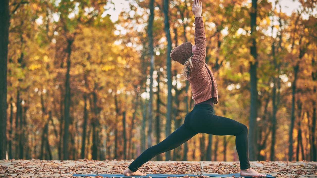 Frau macht in Herbstlandschaft Krieger 1 Yoga-Übung gegen Bluthochdruck