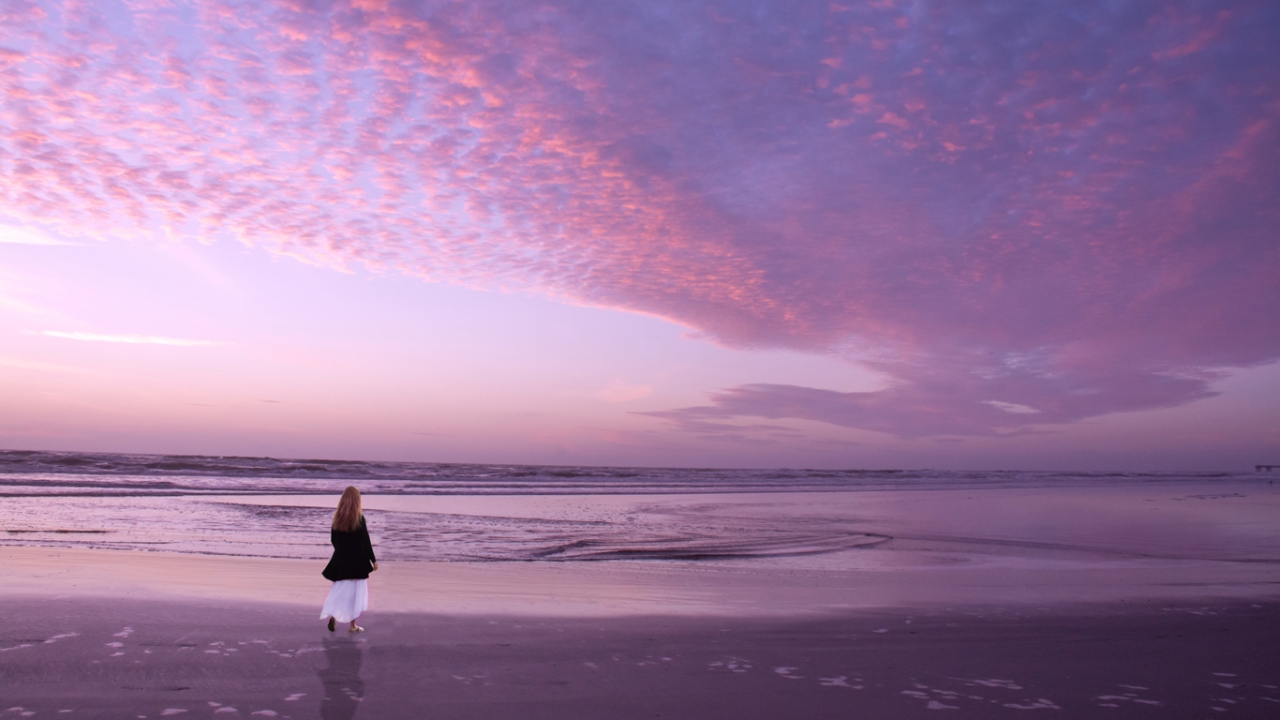Veränderung: Frau läuft nachdenklich am Strand im Sonnenuntergang mit lila Himmel entlang Veränderung: Frau läuft nachdenklich am Strand im Sonnenuntergang mit lila Himmel entlang