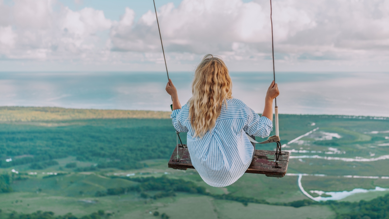 Teaserbild: Eine Frau schaukelt. Vor ihr sieht man die Weiten des Meeres.