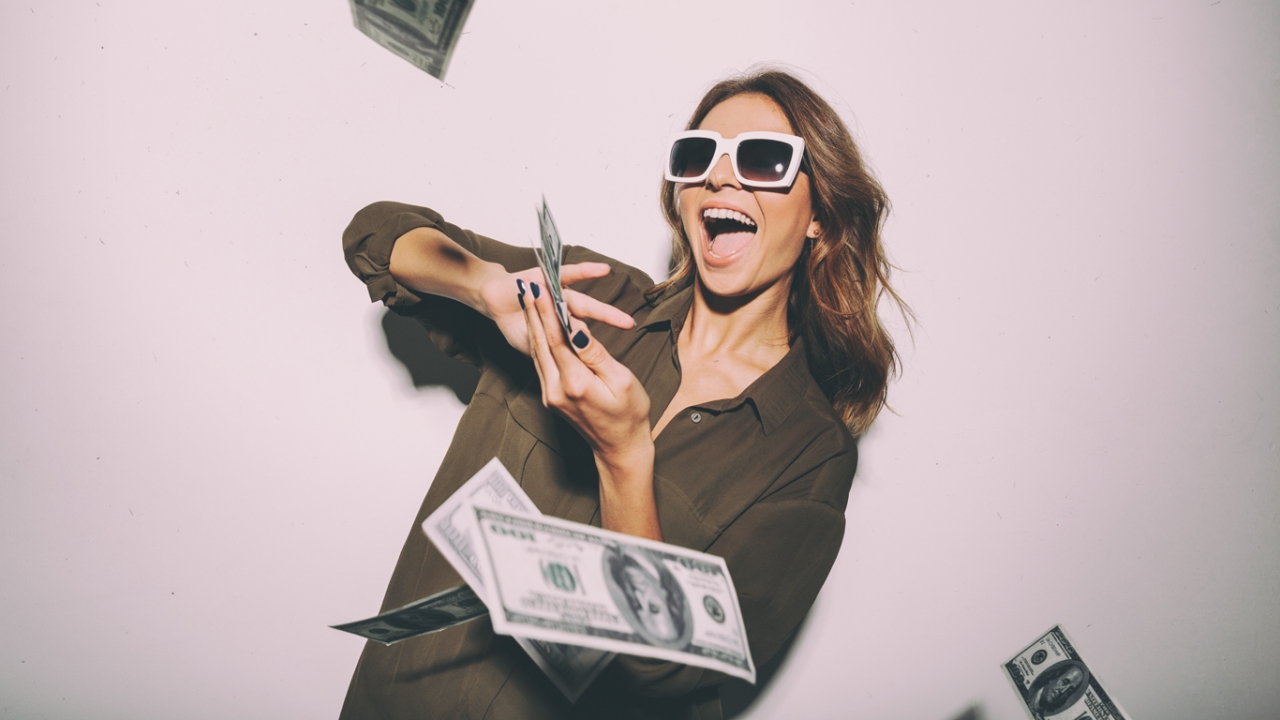 Eine Frau mit Sonnenbrille wirft Geldscheine in die Kamera
