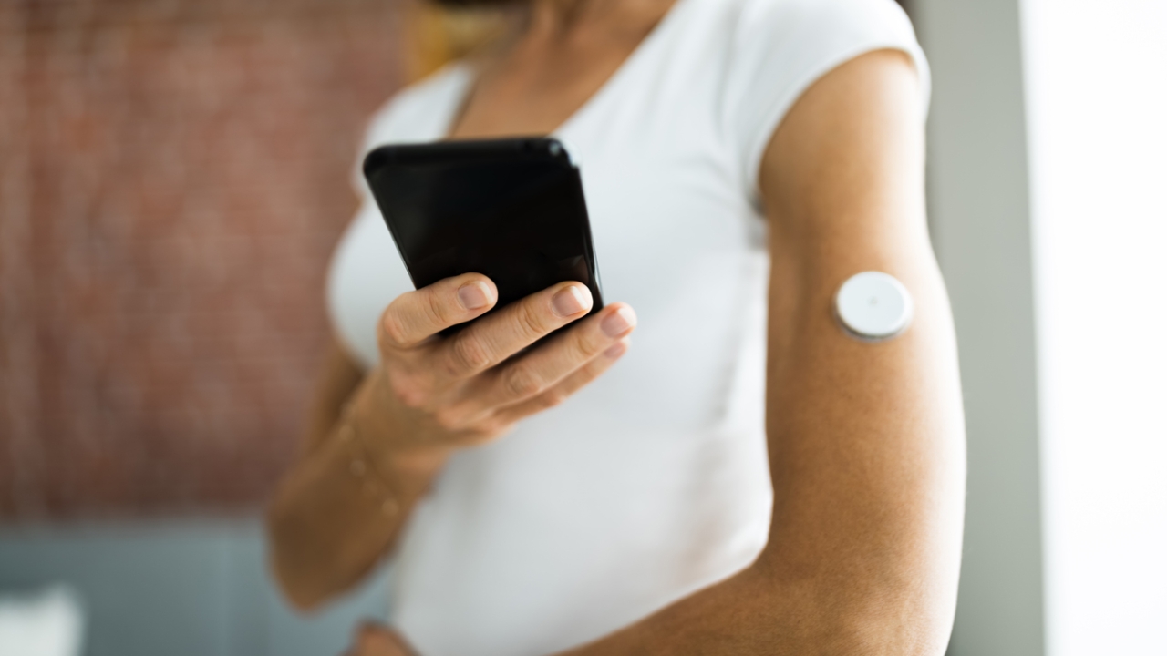 Eine Frau misst mit ihrem Handy und einem Sensor am Arm ihren Blutzucker