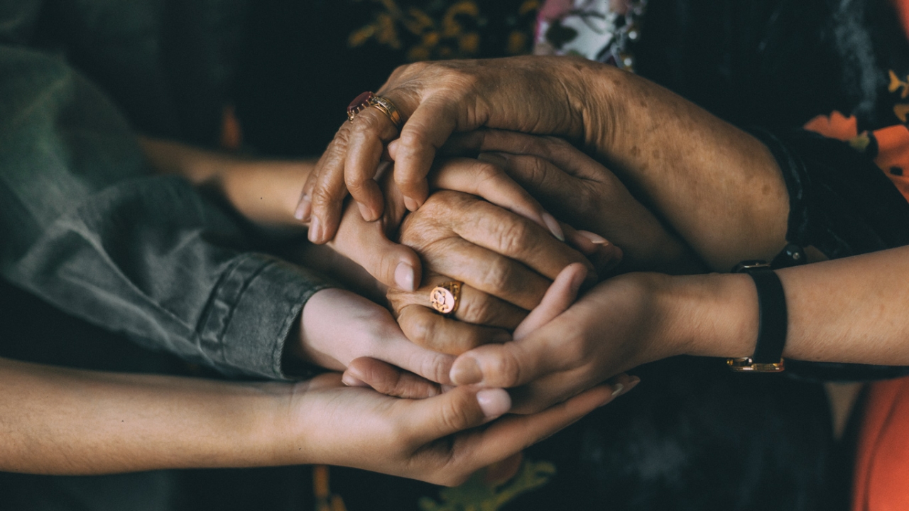 Epigenetik: Wie du ein vererbtes Trauma erkennen und lösen kannst Verschiedene Hände von jungen bis alten Menschen, die sich gegenseitig halten.