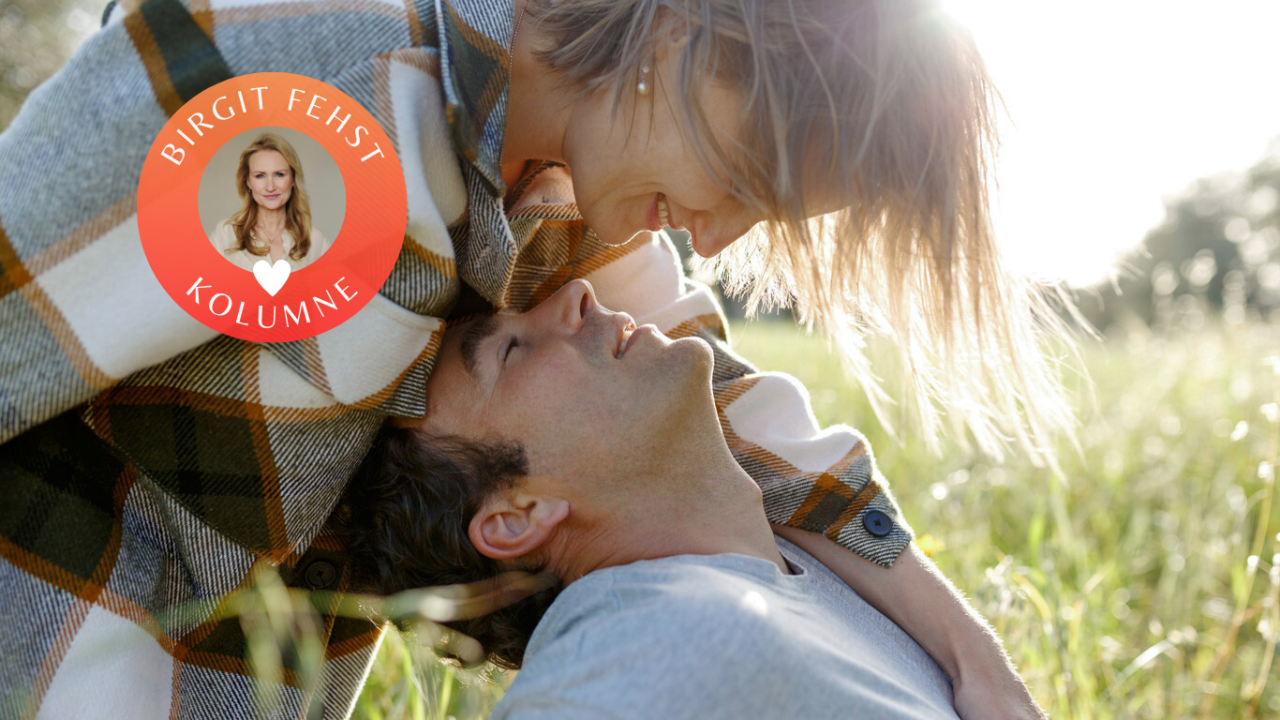 Intimität: Frau beugt sich lächelnd über Mann im Gras liegend