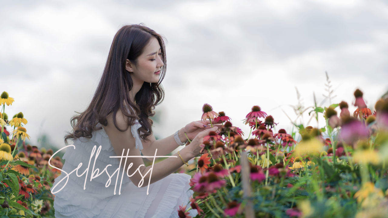 Selbstliebe Test: Frau im weißen Kleid berührt liebevoll Echinacea Blumen im Feld sitzend