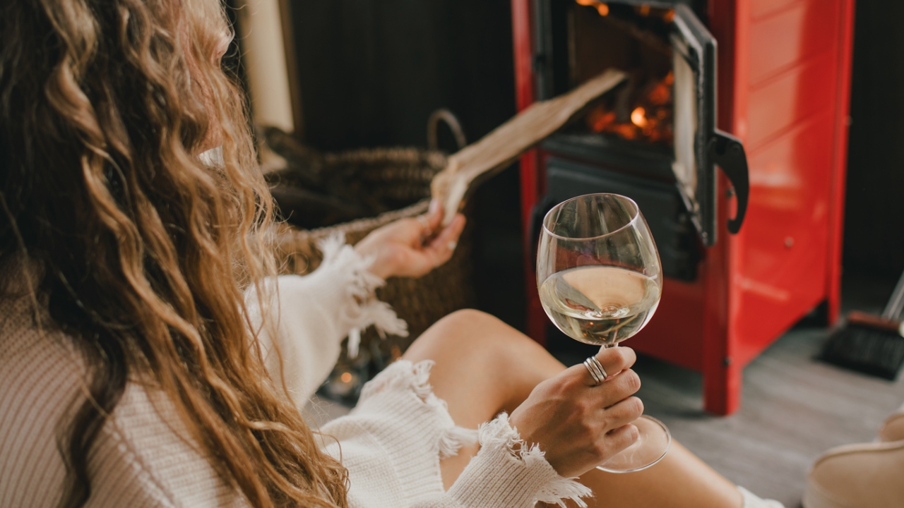 Eine Frau sitzt vor dem Kamin und hält ein Weinglas in der Hand | Leben ohne Alkohol