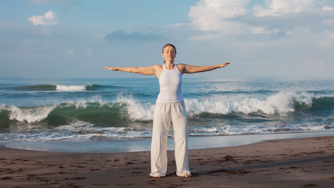 Eine Frau steht mit ausgebreiteten Armen vor einem Meer