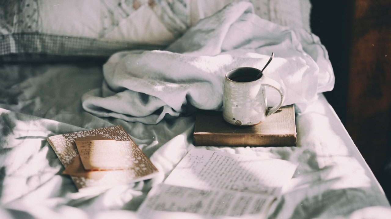Morgenroutine: Ideen für einen guten Start in den Tag Morgenroutine: Tasse Kaffee steht auf einem Journal im Bett