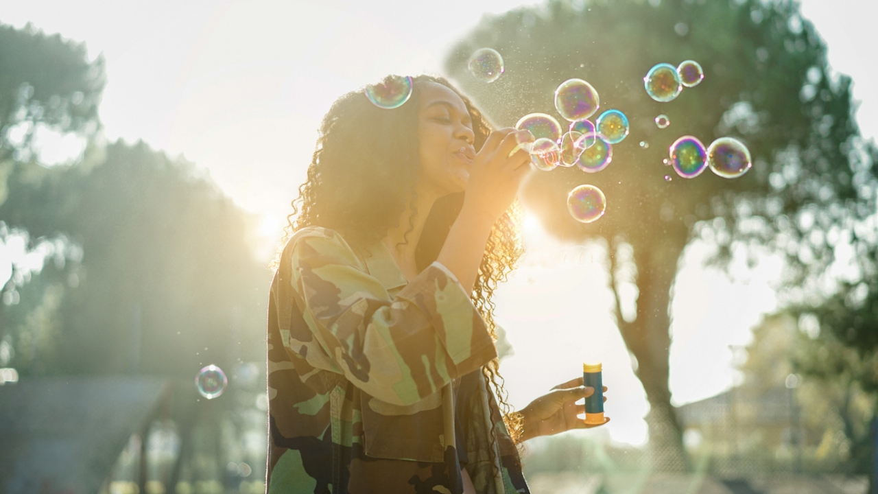 5 Tipps, um negative Gedanken zu stoppen Negative Gedanken stoppen: Eine Frau pustet Seifenblasen in der Sonne und wirkt dabei unbeschwert und fröhlich.