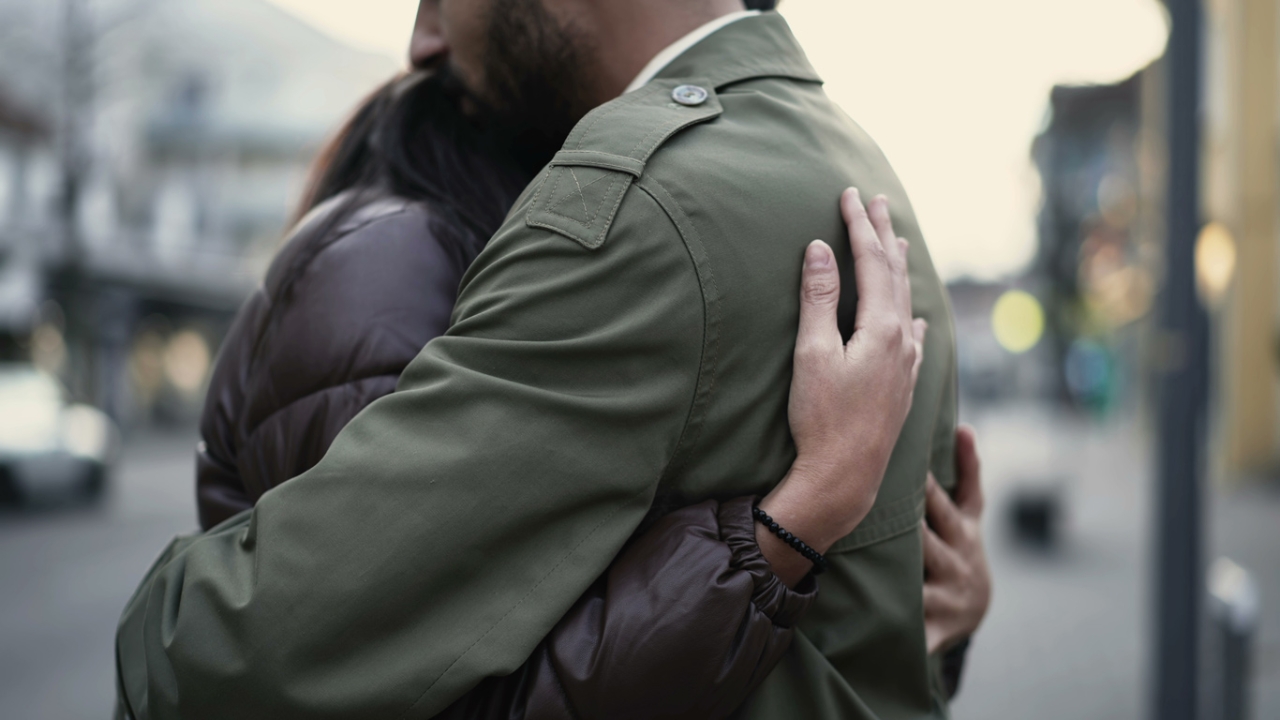 Zwei Menschen umarmen sich auf einer Straße, nur ihre Oberkörper und Kleidung sind zu sehen. | Beziehungen loslassen