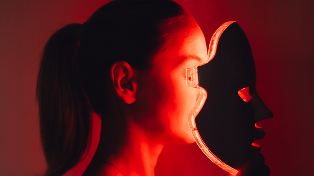 Rotlichttherapie: Eine Frau trägt eine rot leuchtende LED-Lichttherapiemaske in einem dunklen Raum.