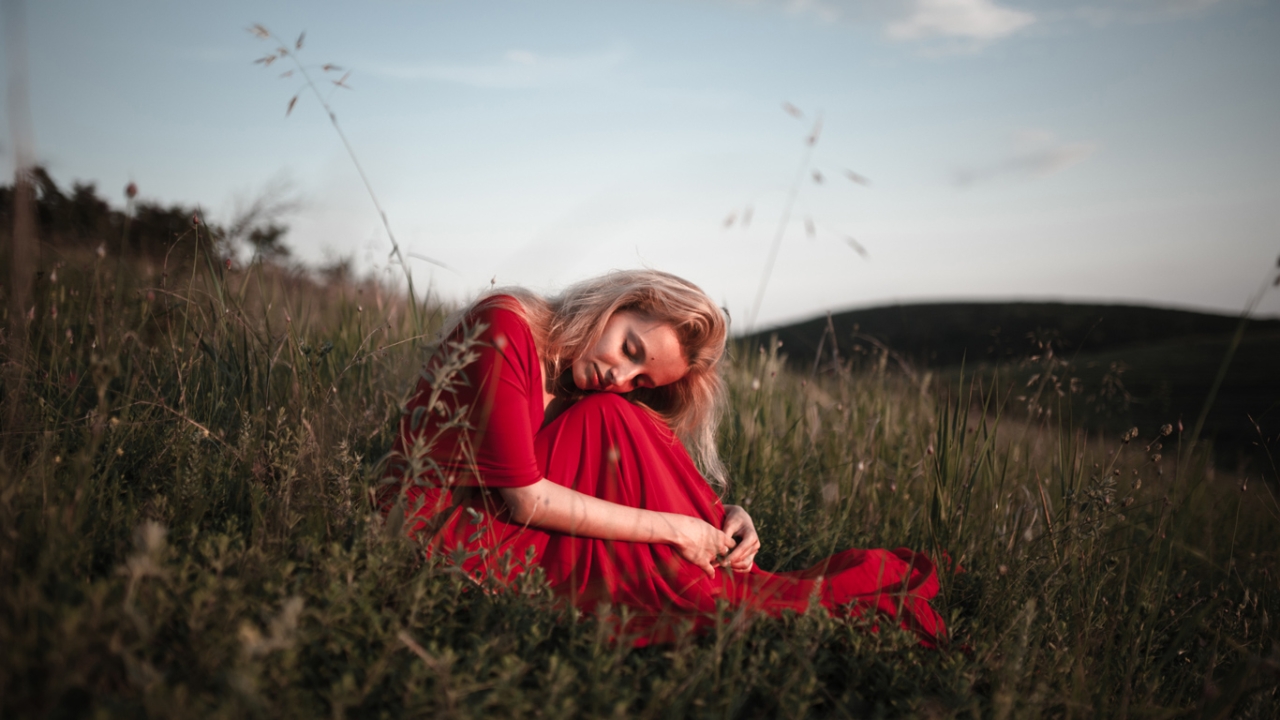 Frau in einem roten Kleid sitzt im Gras und legt den Kopf auf ihre Knie. | 7 Säulen der Resilienz
