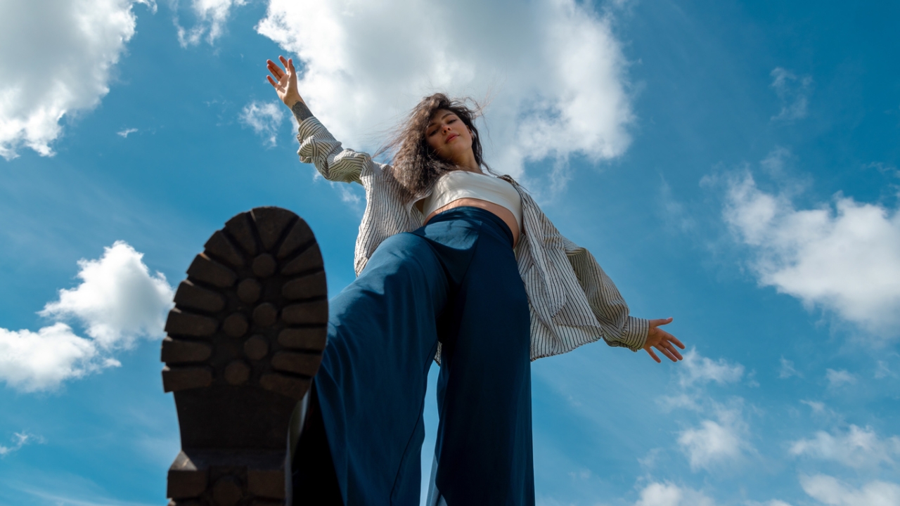 Quarterlife Crisis: Eine Frau, von unten vor blauem Himmel fotografiert, streckt Fuß nach vorne, die Arme ausgebreitet.