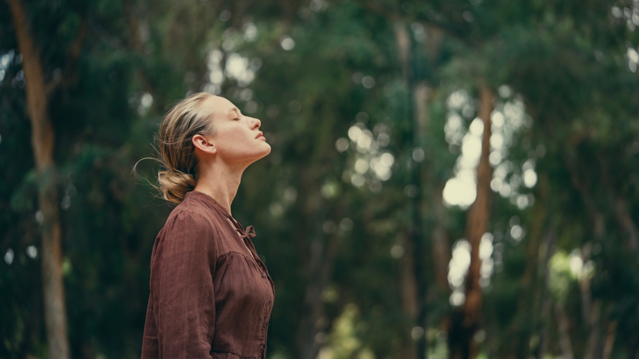 Frau mit geneigtem Kopf und geschlossenen Augen vor Waldhintergrund