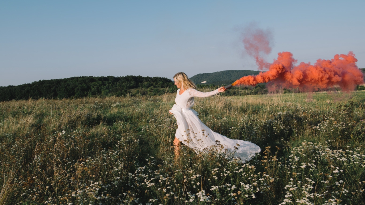 Frau in weißem Kleid rennt mit Kreidepulver in der Hand über eine Wiese